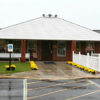 A small brick building with a white fence and yellow flowers lining the entrance, set on a rainy day.