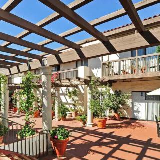 A sunny courtyard with a wooden pergola, decorated with potted plants and balconies.