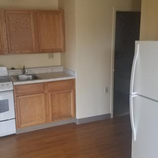A small kitchen with wooden cabinets, a white refrigerator, stove, and sink.