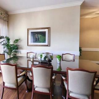 A well-decorated dining room featuring a polished wooden table, elegant chairs, a potted plant, and framed artwork on the wall.
