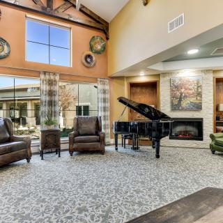 A modern living room featuring a grand piano, fireplace, and large windows allowing natural light.