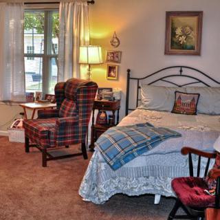 A cozy bedroom with a bed, a plaid armchair, and a lamp by the window.