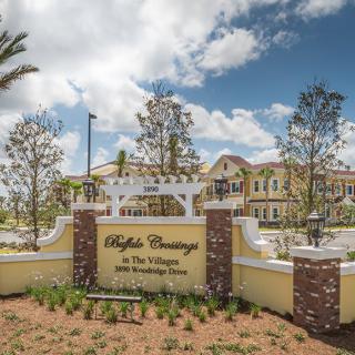 A scenic view of a building with a welcoming sign in the foreground and trees under a blue sky with clouds.