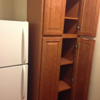 A kitchen corner with a white refrigerator next to a tall wooden cabinet with open shelves.