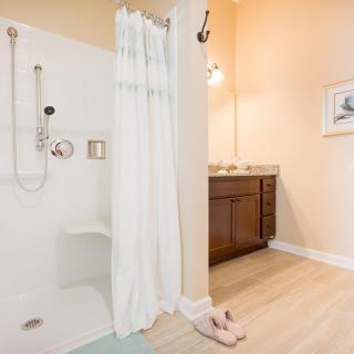 A clean and modern bathroom featuring a shower with a white curtain, a wooden vanity with a mirror above, and light wood flooring.