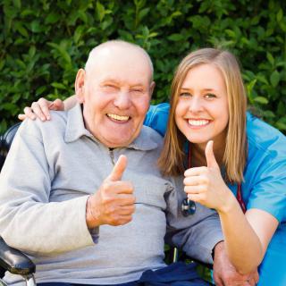 A smiling elderly man and a nurse giving thumbs up outdoors.