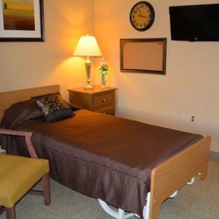 A cozy bedroom featuring a single bed, a bedside lamp, and a wall-mounted television.