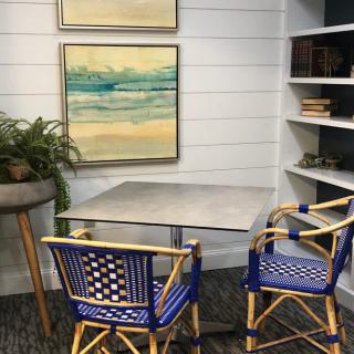 A cozy corner with a small table, two stylish chairs, artwork on the wall, and a bookshelf.