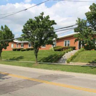 A row of suburban houses with a well-kept lawn and trees lining a residential street.