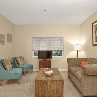 A cozy living room with a sofa, chairs, and a coffee table, featuring a TV and floor lamp.