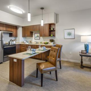 A modern kitchen and dining area with wooden cabinetry, a small dining table with upholstered chairs, and contemporary decor.