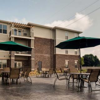 Outdoor patio area with tables, chairs, and umbrellas adjacent to a multi-story building.