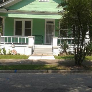 A green house with a welcoming front porch surrounded by trees.