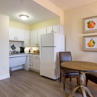 A small kitchen area with white cabinets and a dining table with chairs.