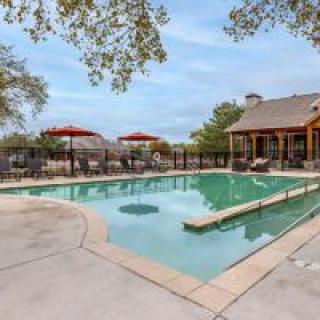 An outdoor swimming pool area with lounge chairs and umbrellas, set against a backdrop of trees and a clear sky.