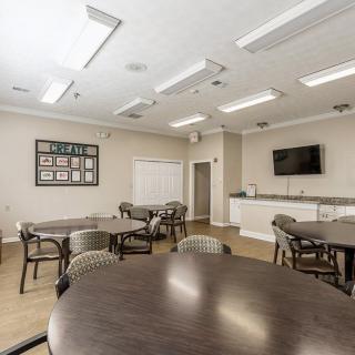 A modern conference room with multiple tables and chairs, equipped with a television and bright lighting.