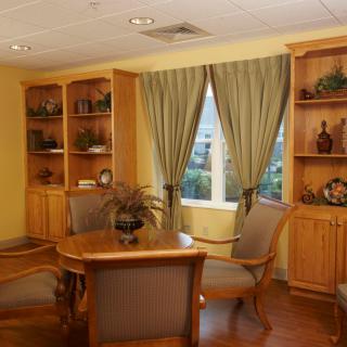 A cozy office space with wooden shelves, a table, and chairs by a window with curtains.