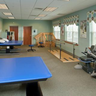 A rehabilitation center room equipped with therapy tables and parallel bars for physical therapy sessions.
