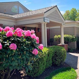 A charming house exterior with vibrant pink flowers and neatly trimmed bushes.