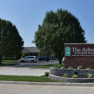 Entrance sign for 'The Arbors' with a landscaped driveway and trees.