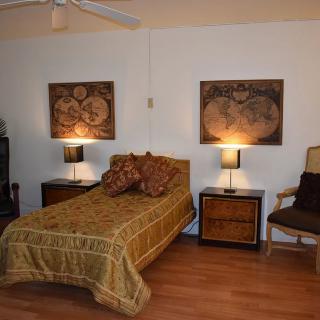 A cozy bedroom featuring a single bed with warm-toned bedding, flanked by two nightstands with lamps and decorative wall art above.