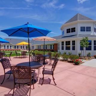 A sunny outdoor patio with tables, chairs, and colorful umbrellas in front of a large building.