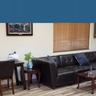 A cozy living room with a dark leather sofa, wooden tables, and decorative artwork on the walls.