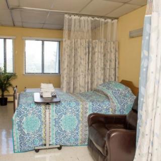A hospital room with a bed and chair, separated by curtains.