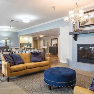 A stylish living room featuring a yellow sofa, blue ottoman, elegant chandelier, and a cozy fireplace.