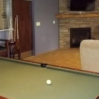 A cozy living room with a billiard table, pool cues, fireplace, and a television.