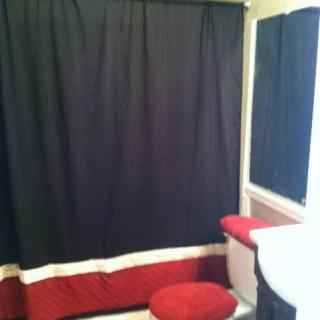 A bathroom with a black and red color scheme, featuring a shower curtain and toilet cover.