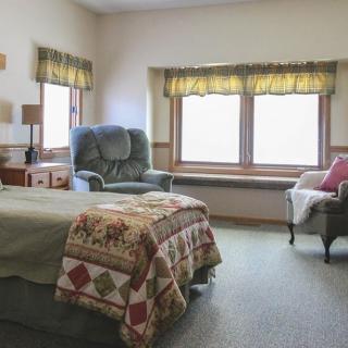 A cozy bedroom with a bed, armchair, and large windows letting in natural light.