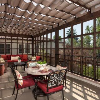 A cozy outdoor patio with a pergola, featuring a dining set with red-cushioned chairs and surrounding seating.
