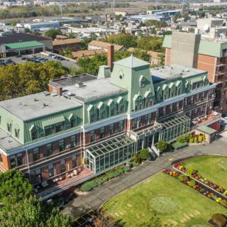Aerial view of a large building with green rooftops and an adjacent garden in an urban setting.