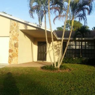 A residential house with palm trees and a well-maintained lawn in sunlight.
