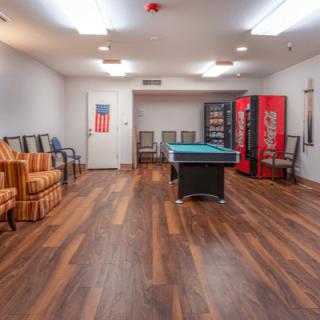 A game room with a pool table, vending machines, and seating on a wooden floor.