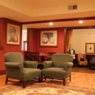 A cozy living room with green armchairs and wall art under warm lighting.