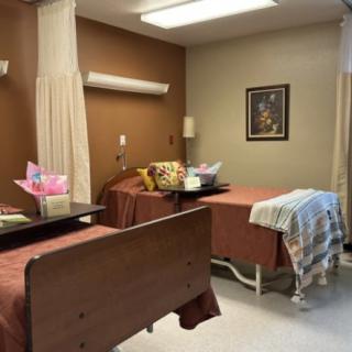 A hospital room with two beds, divider curtains, and decorative flowers and artwork.