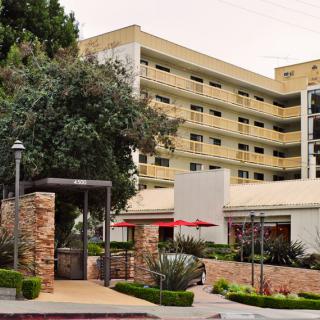 A modern hotel building with balconies, surrounded by trees and landscaping.