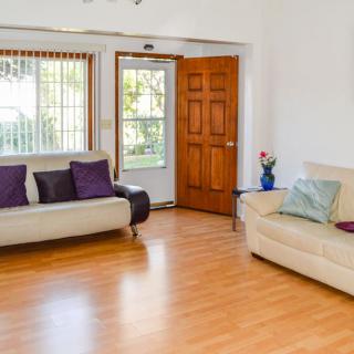 A cozy living room with wooden flooring, featuring two sofas adorned with colorful cushions and an open door letting in natural light.