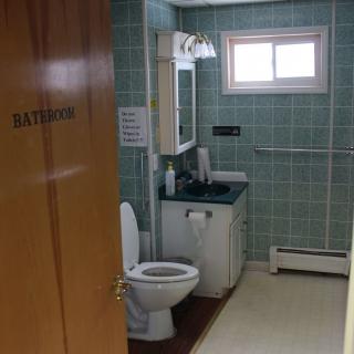 A bathroom with a toilet, sink, and mirror, featuring tiled walls and a small window.