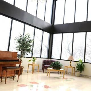 A bright, spacious room with large windows, featuring a piano and some plants.