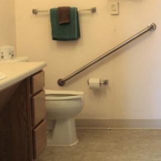 An accessible bathroom with a grab bar next to the toilet and towels neatly hung on the wall.