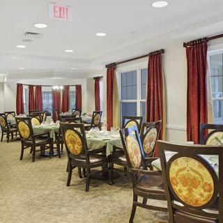 An elegant dining room with multiple tables and chairs, featuring warm lighting and red curtains.
