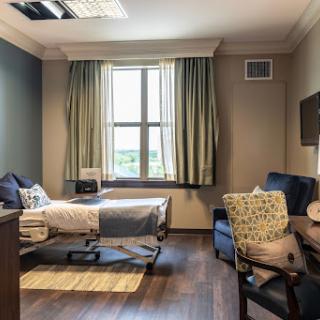 A well-lit and modern hospital room featuring a patient bed, comfortable seating, and large windows.