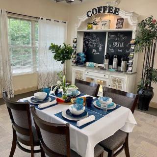 A cozy dining area with a neatly set table and a charming coffee station, surrounded by plants and natural light.