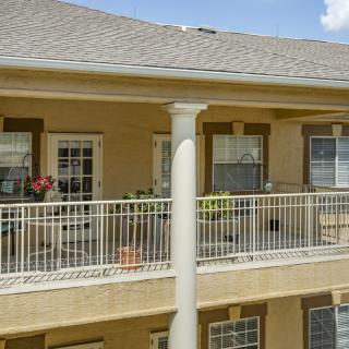 A view of a residential apartment balcony with outdoor seating and decorative plants.