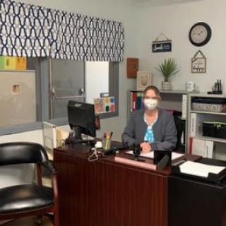 An individual wearing a mask sitting at their desk in an office setting.