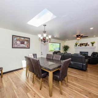 A modern open-concept dining and living area with hardwood floors, featuring a large table, comfortable seating, and natural light from a skylight.