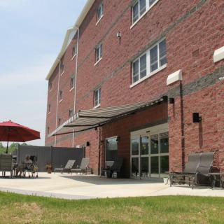 A brick building with an outdoor patio featuring chairs and a red umbrella.